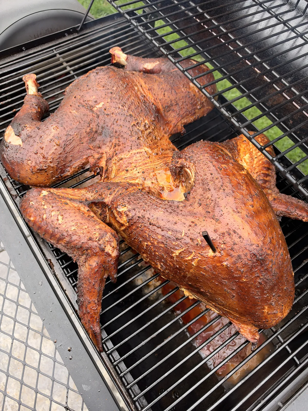 Two Cajun seasoned frog-style turkeys smoking on grill grates with deep mahogany bark from applewood smoke