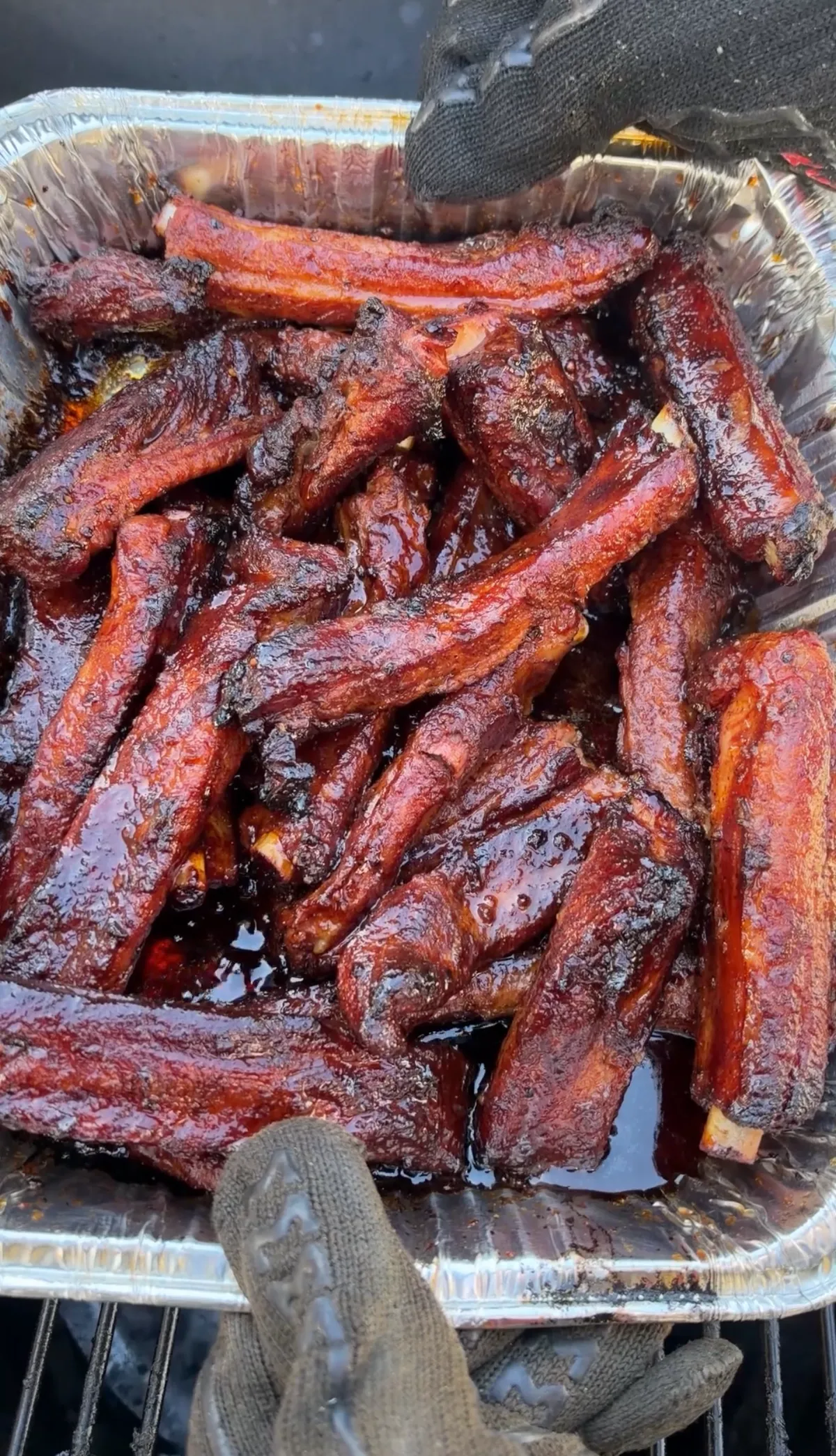 Sticky smoked barbecue party ribs piled in an aluminum foil tray with glossy honey brown sugar BBQ sauce glaze