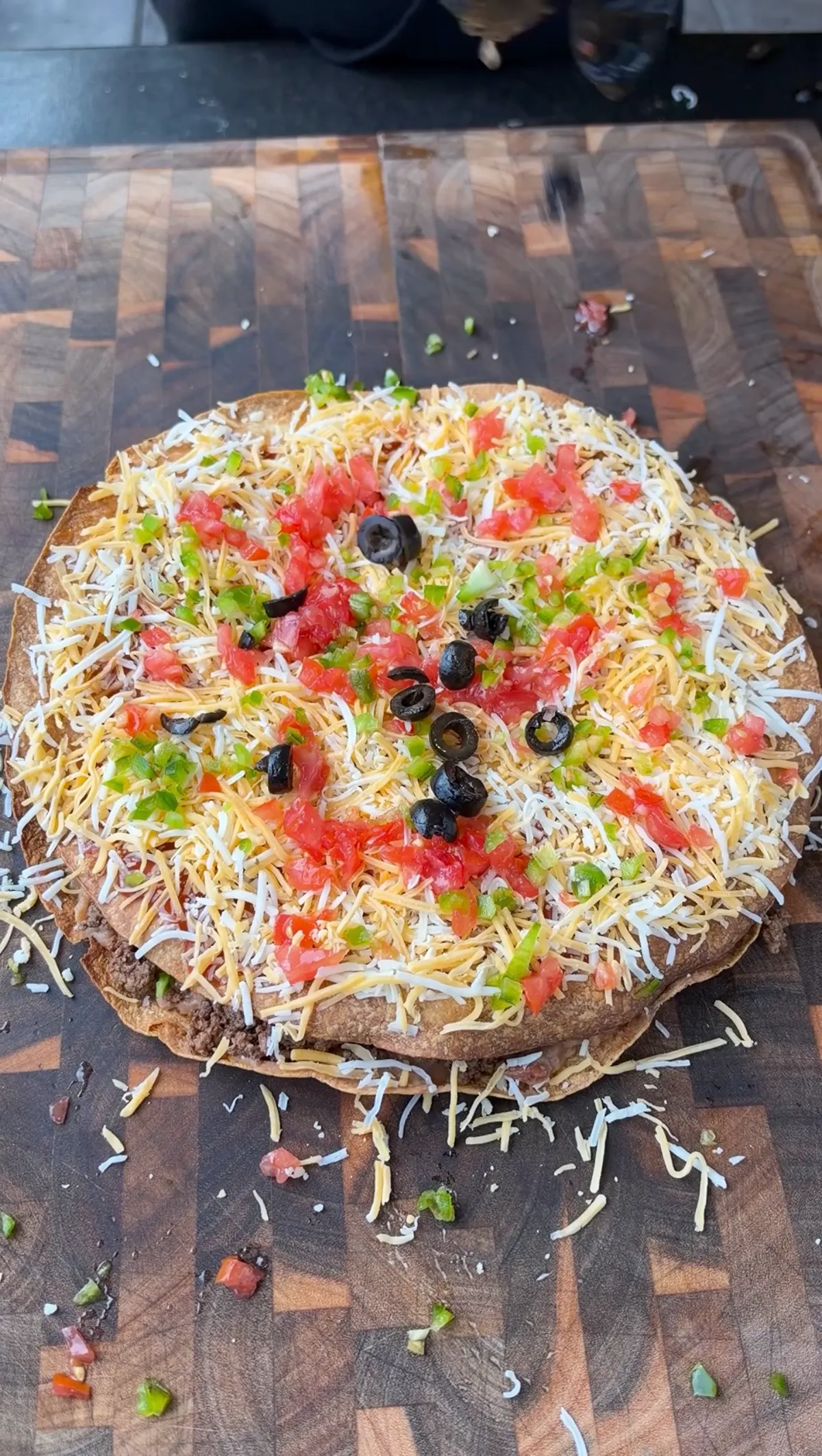 Assembled taco bell mexican pizza copycat topped with shredded Colby Jack, diced tomatoes, black olives and jalapeño before the melt