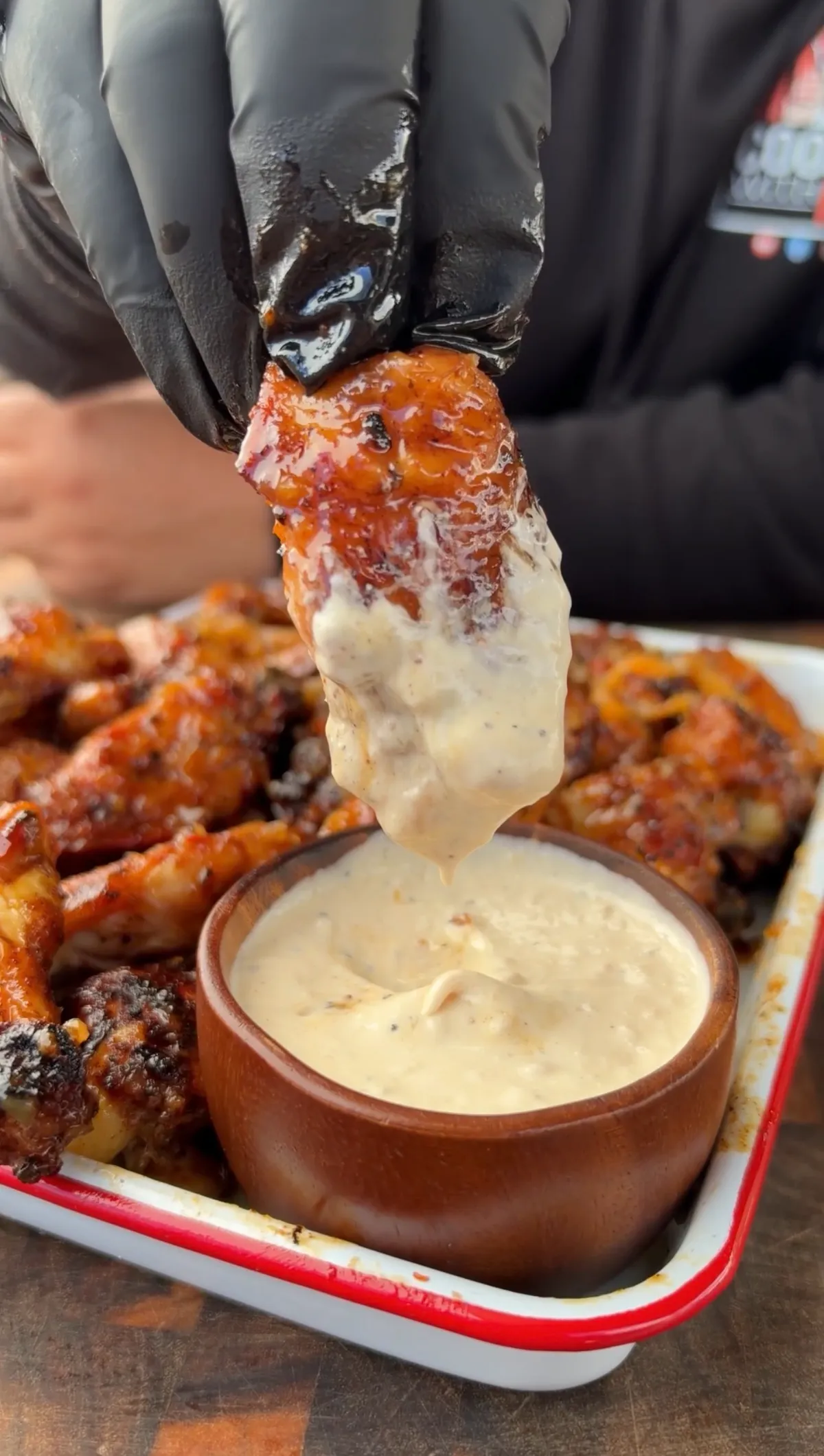 Glazed pineapple habanero chicken wing being dipped into creamy ranch dressing, dripping over a wooden bowl