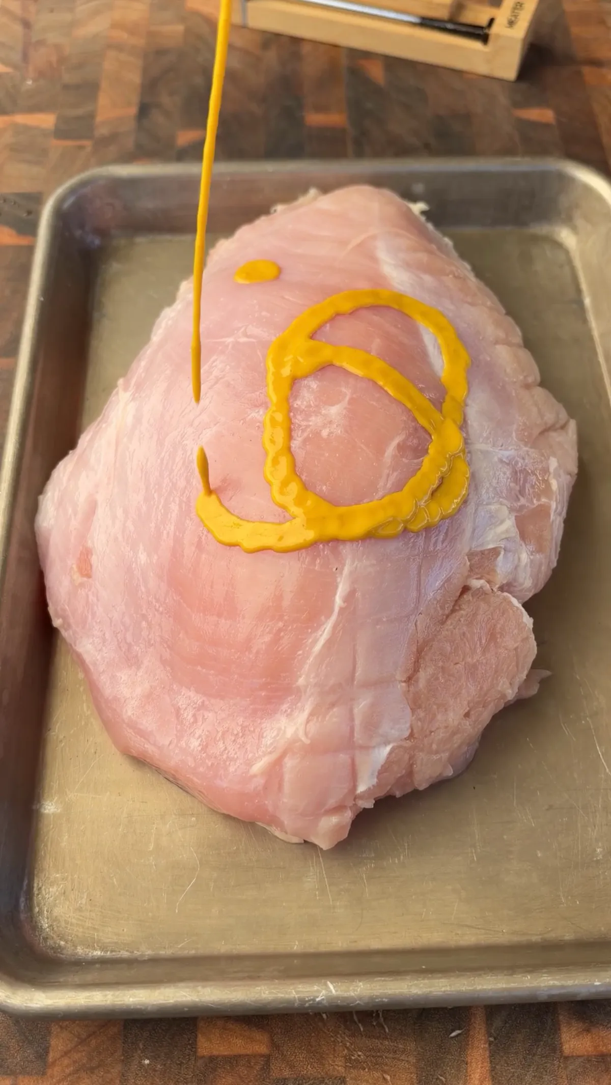 Yellow mustard being drizzled onto a raw boneless turkey breast on a metal sheet pan as a binder before seasoning